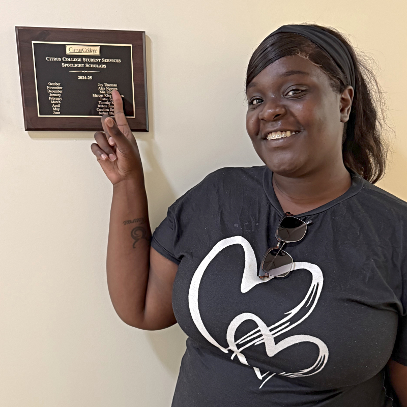 Joy Thurman pointing to her name engraved on a student services "Spotlight Scholars" plaque